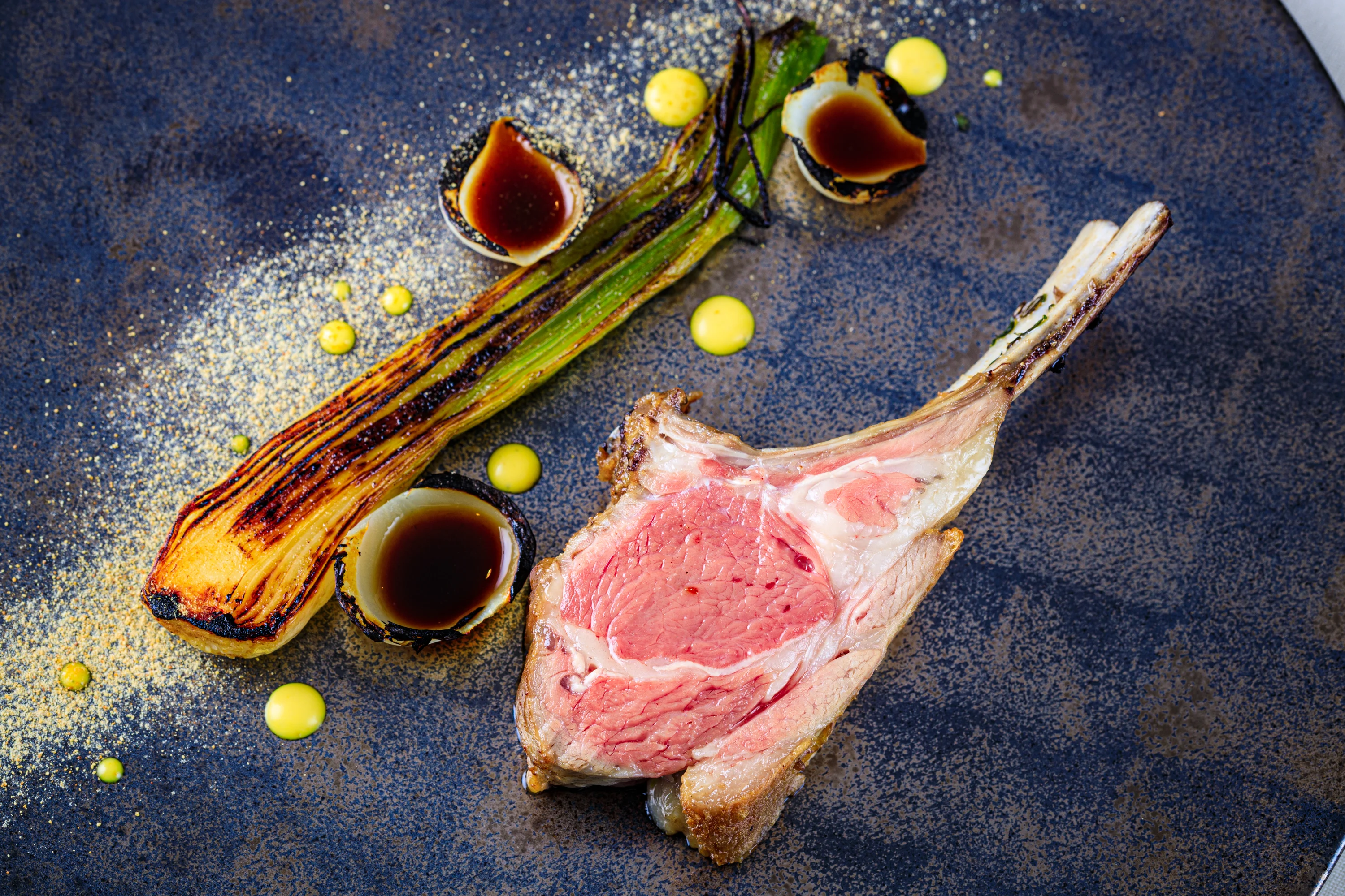 A lamb chop plated with vegetables, sauces and bright green accents.