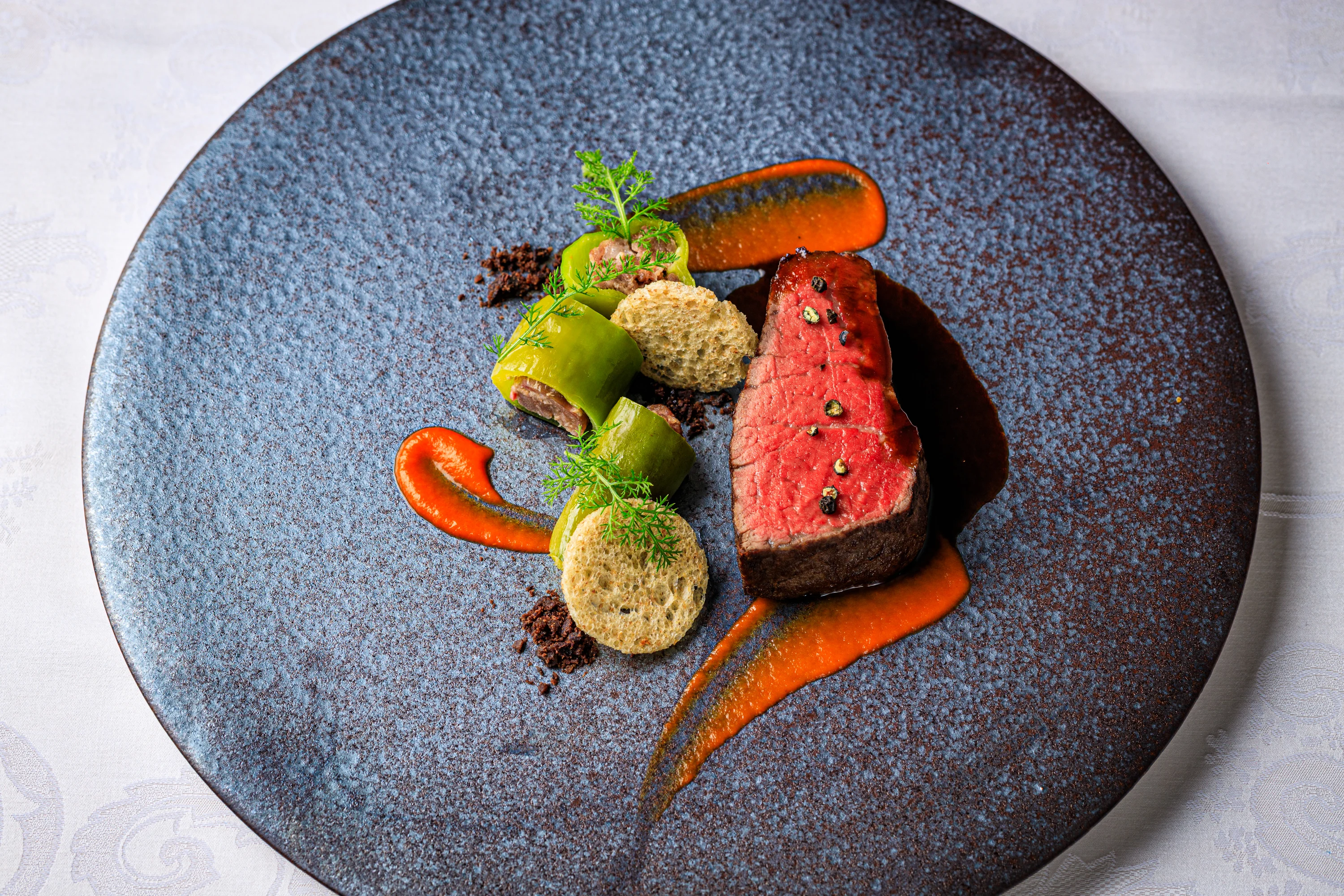 Sliced meat with seasonal vegetables on a dark ceramic plate.