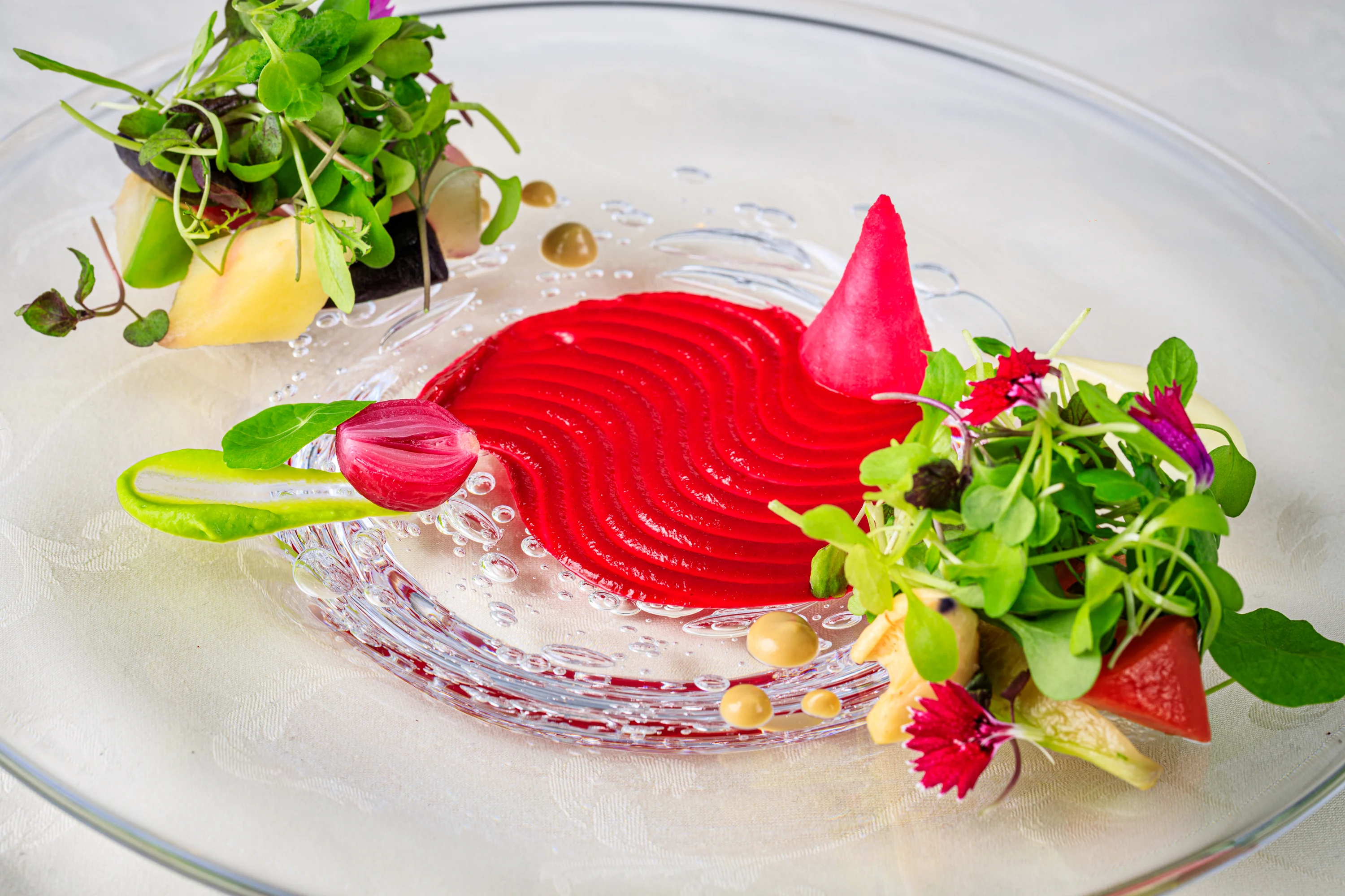 A vivid red plated dish with vegetables, herbs and flowers.