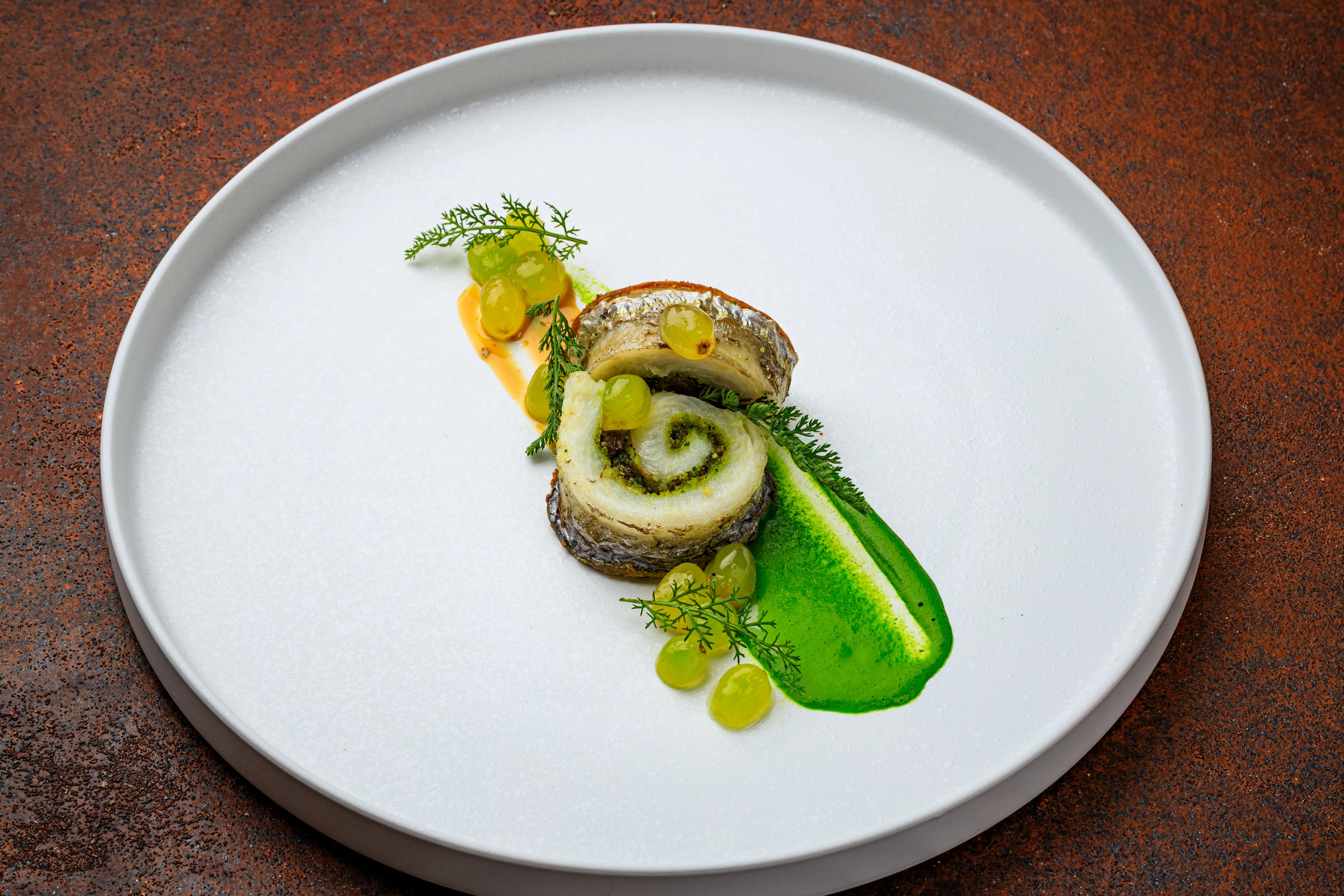 A rolled fish course with vivid green sauce and delicate garnishes.