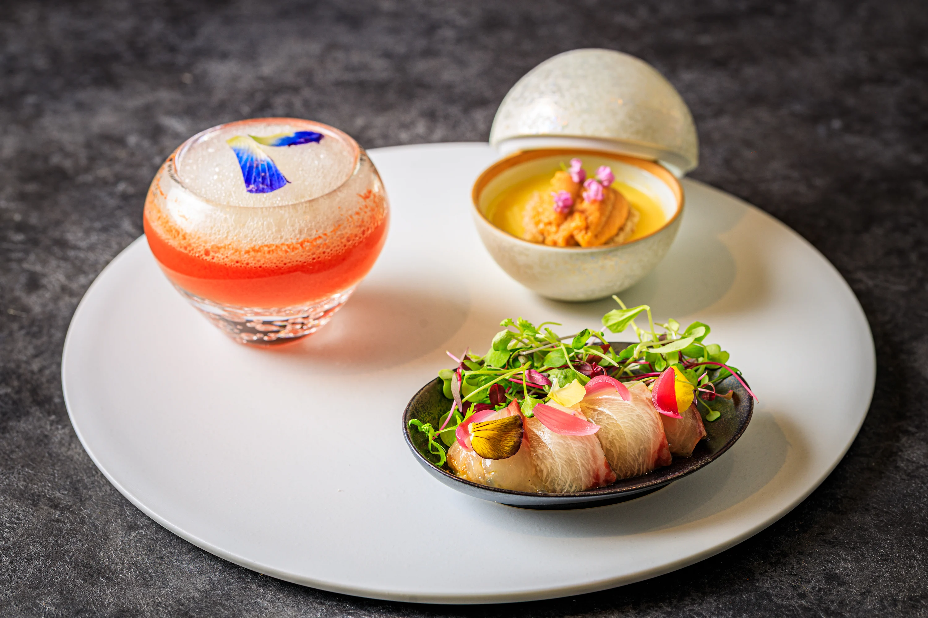 Three small appetizers arranged on a round gray plate.