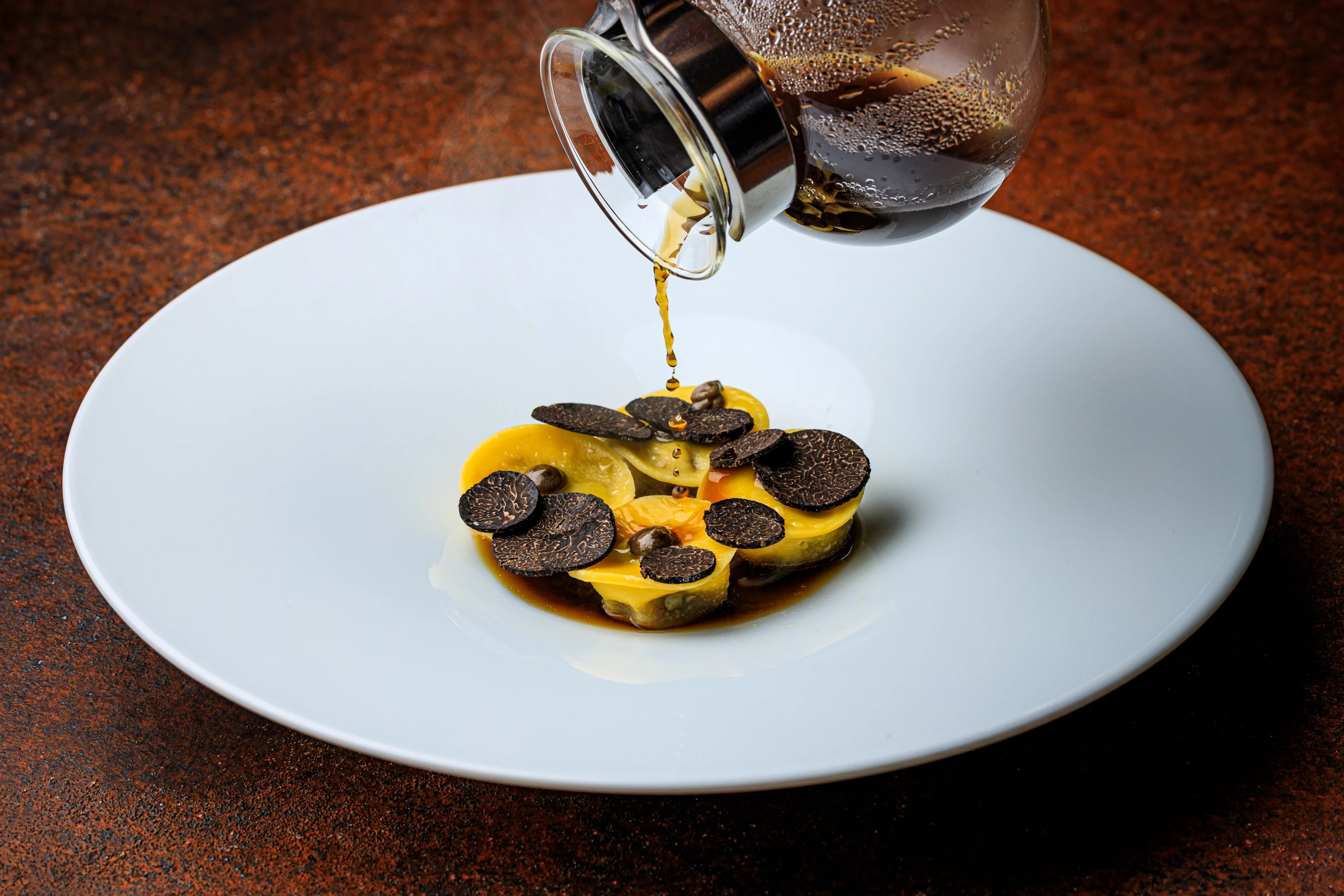 A truffle-topped course finished tableside with a dark sauce.