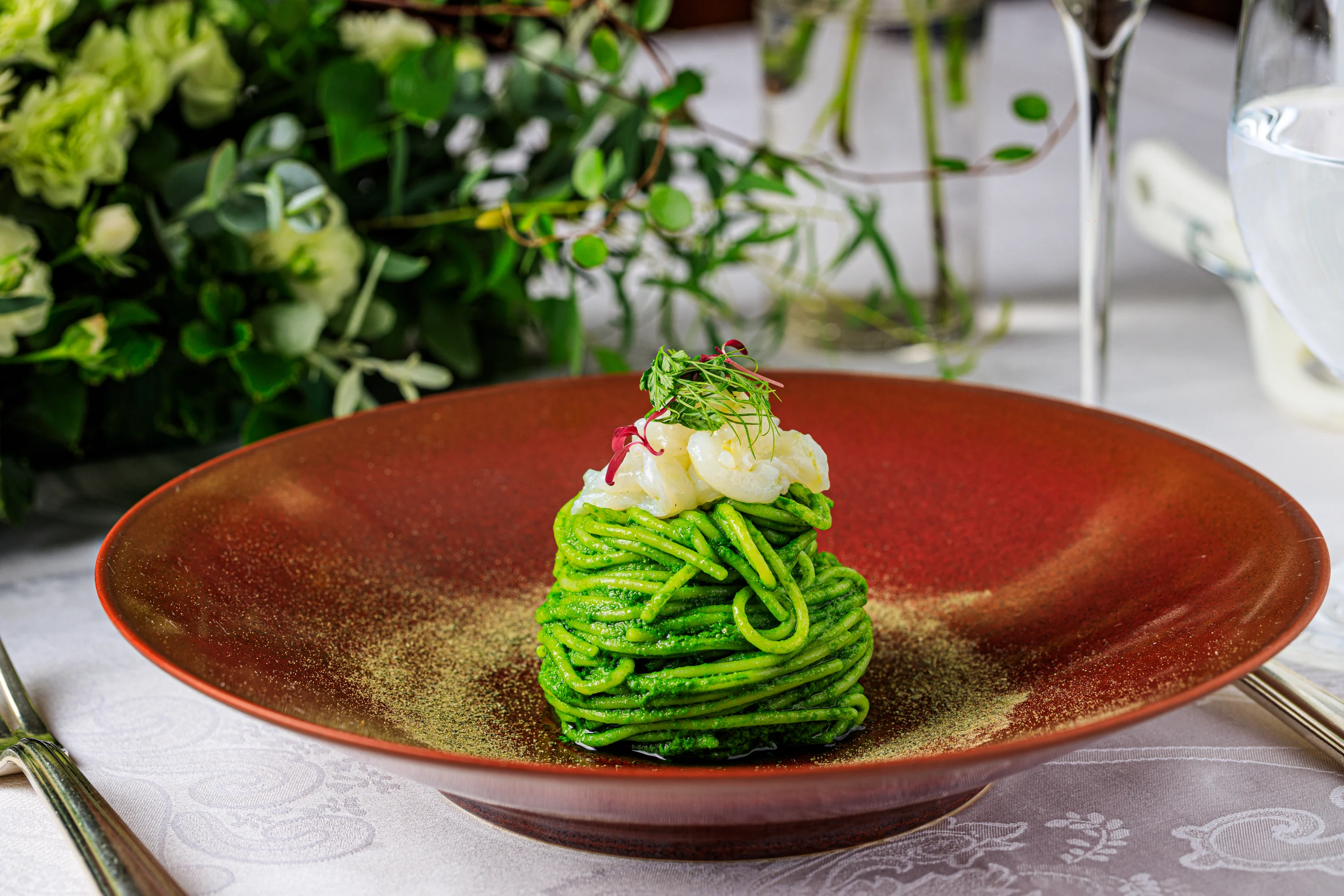 A glass bowl holding a refined seafood and herb course.
