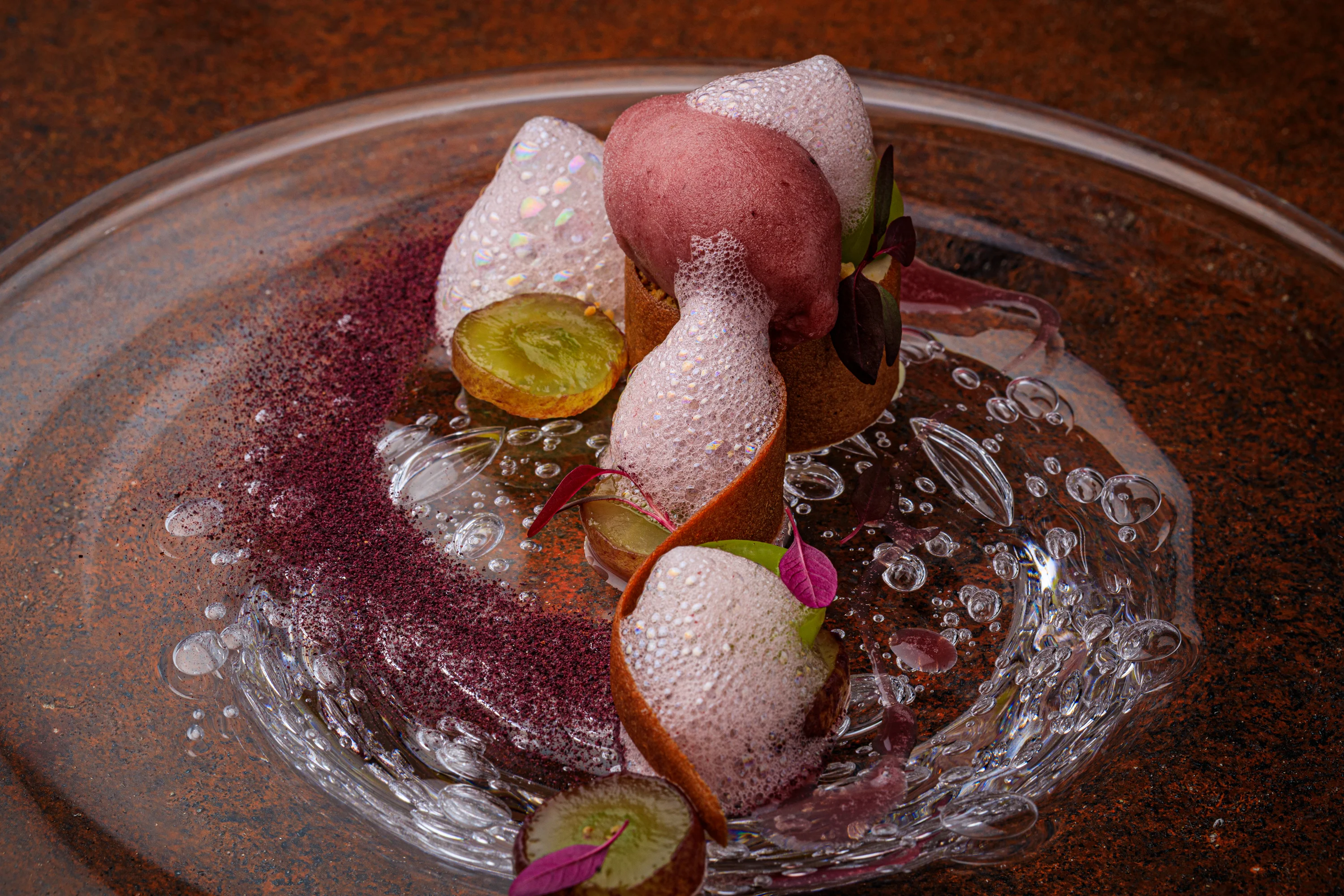 A berry dessert with sorbet, meringue and edible flowers in a glass bowl.