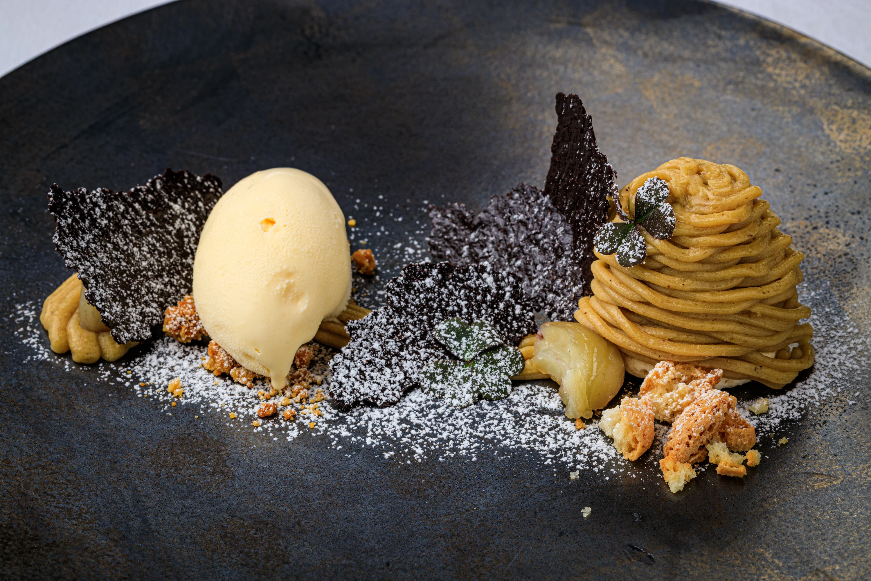 A composed chestnut dessert with ice cream and dark crisp elements.