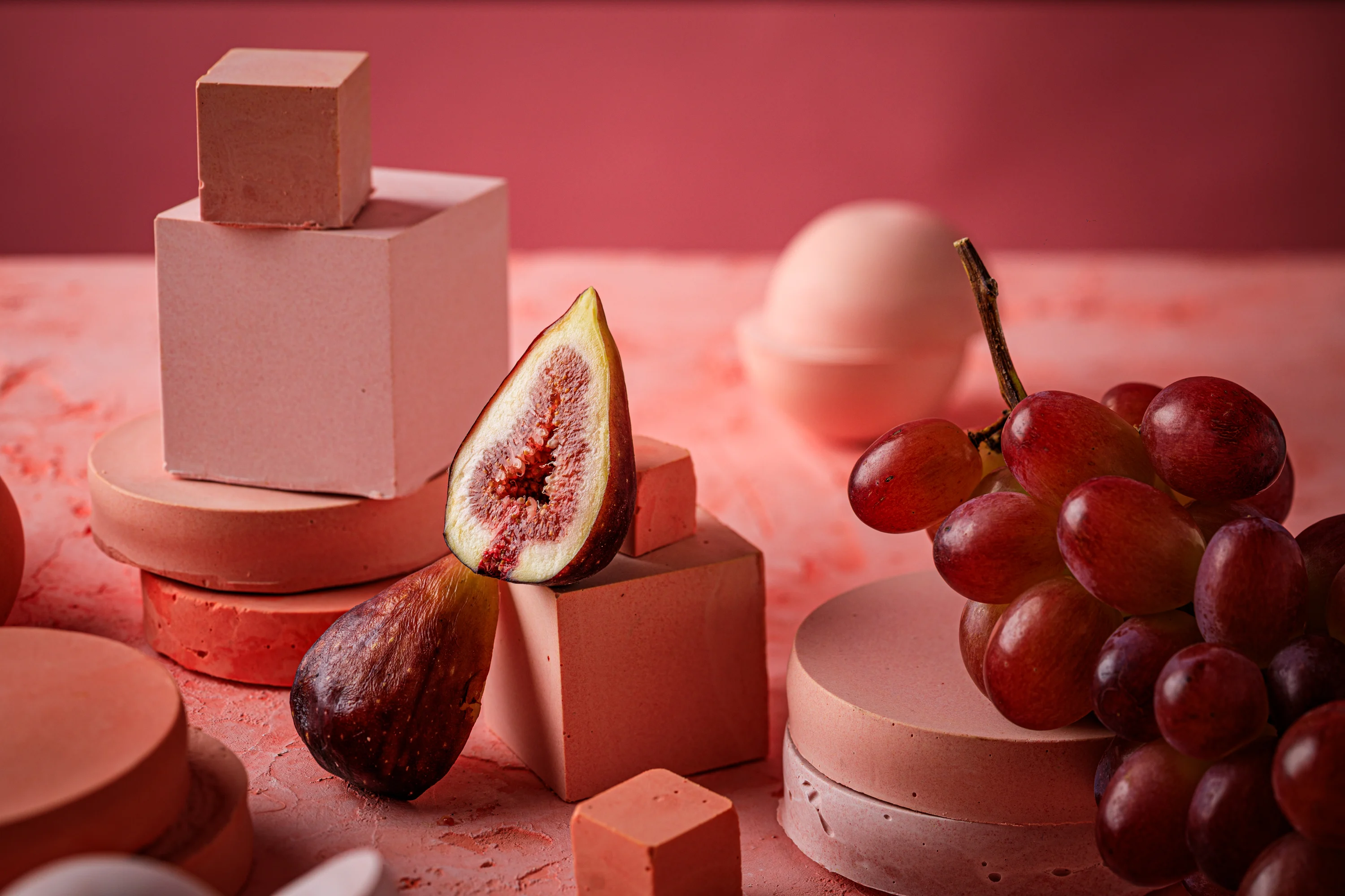 A pink still life of geometric sweets, figs and red grapes.