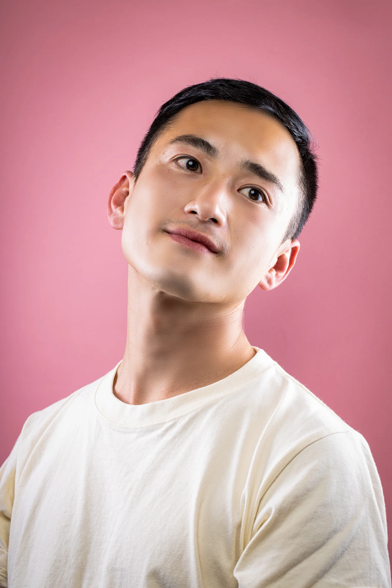 A man looking upward in a softly lit pink studio portrait.