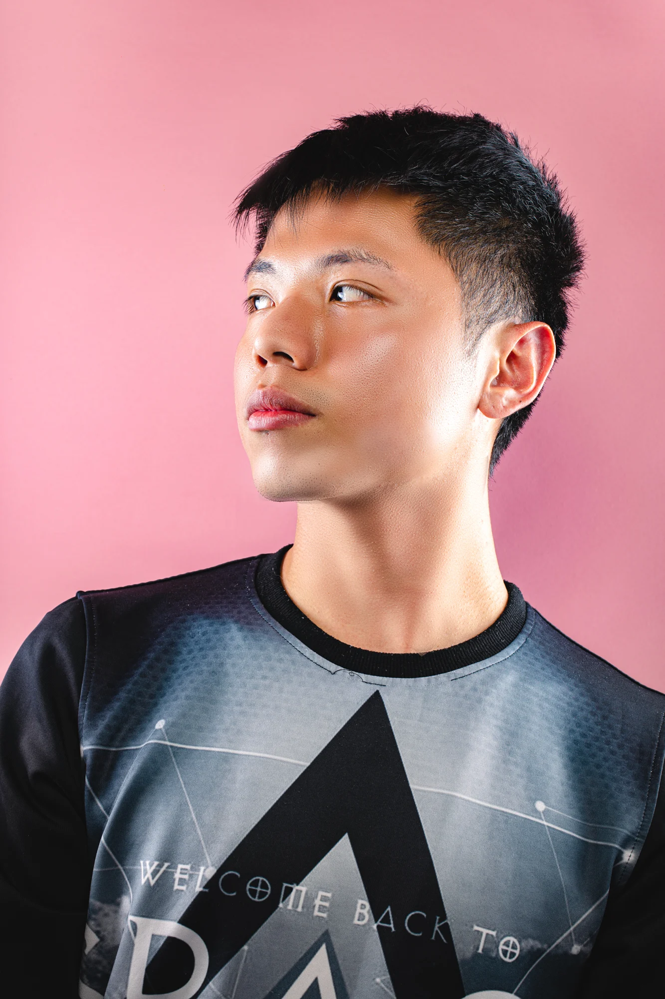 A young man in a graphic shirt photographed against a pink background.