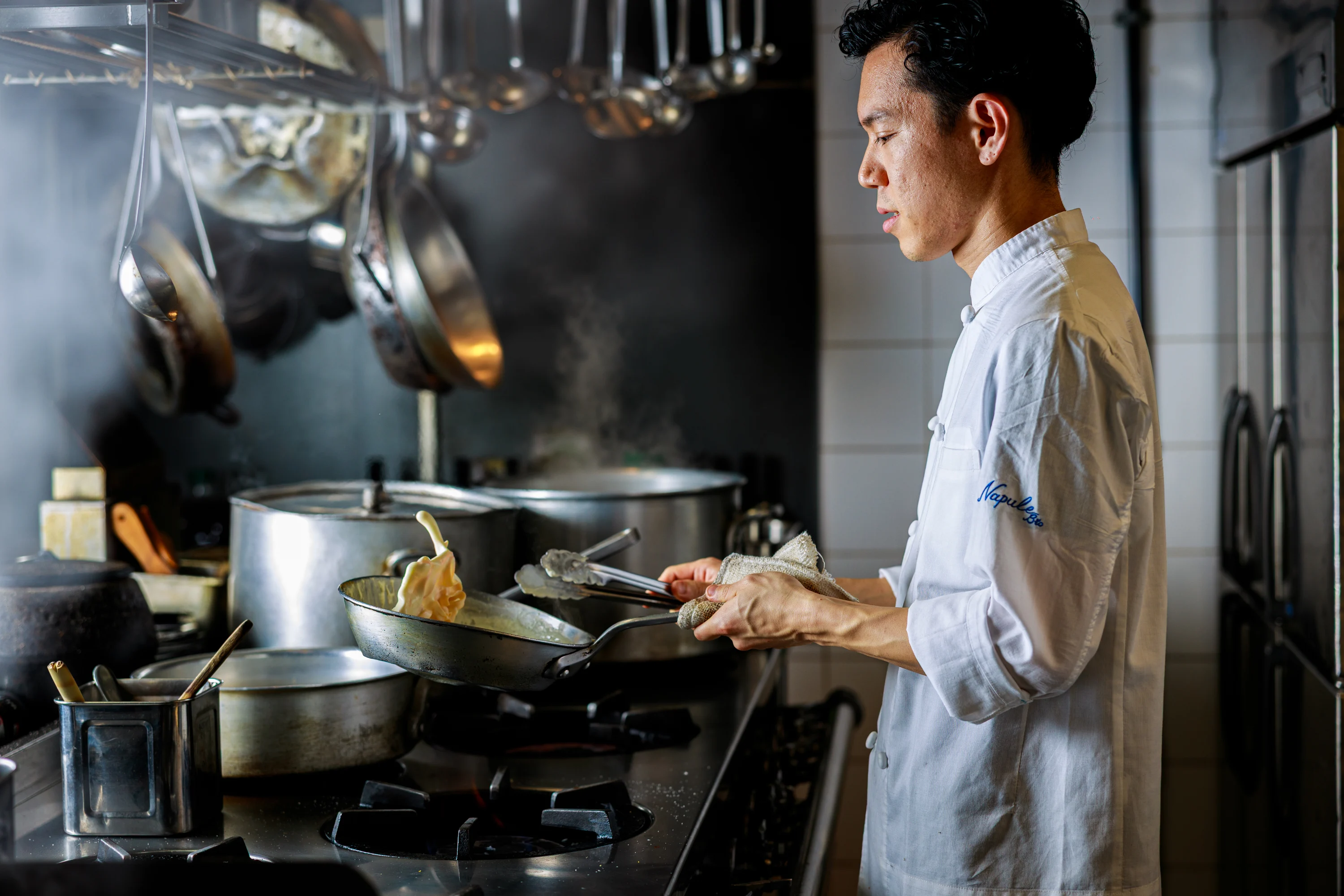A chef cooking at the stove in a professional kitchen.