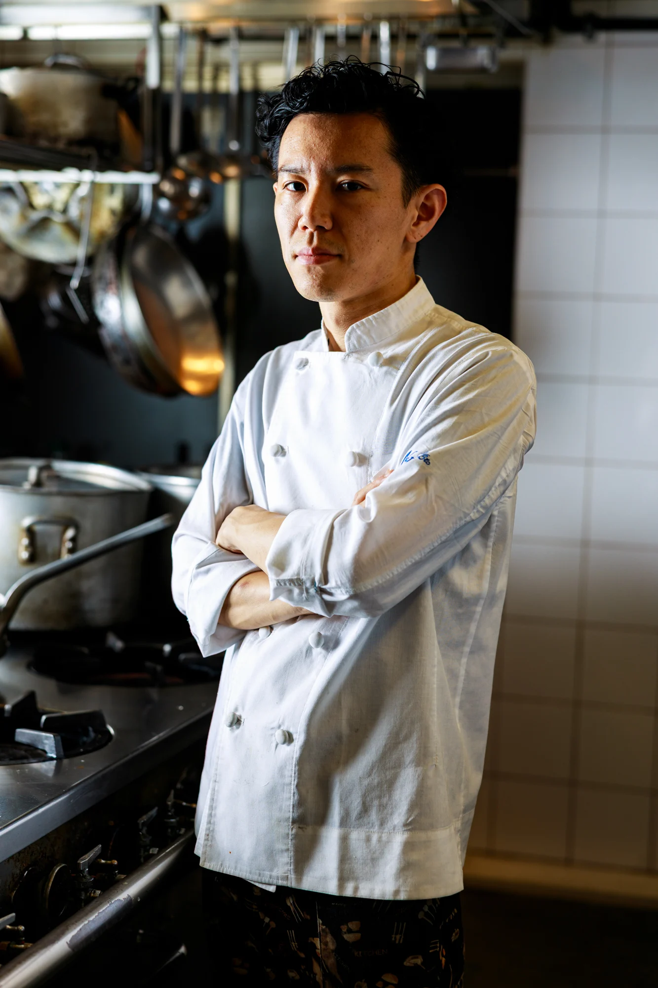 A chef standing with folded arms in a working kitchen.