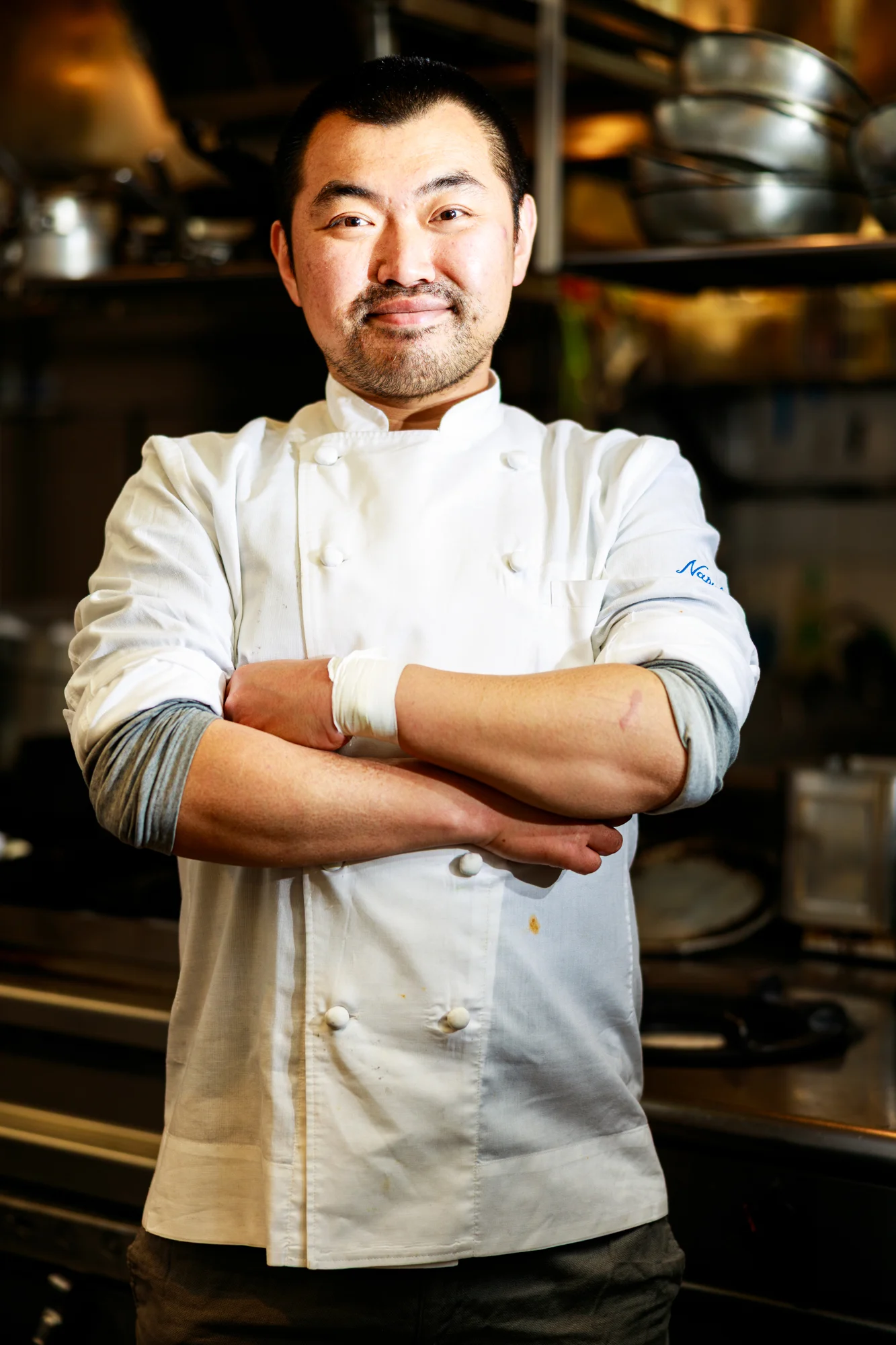 A chef portrait made among the pans and equipment of a restaurant kitchen.