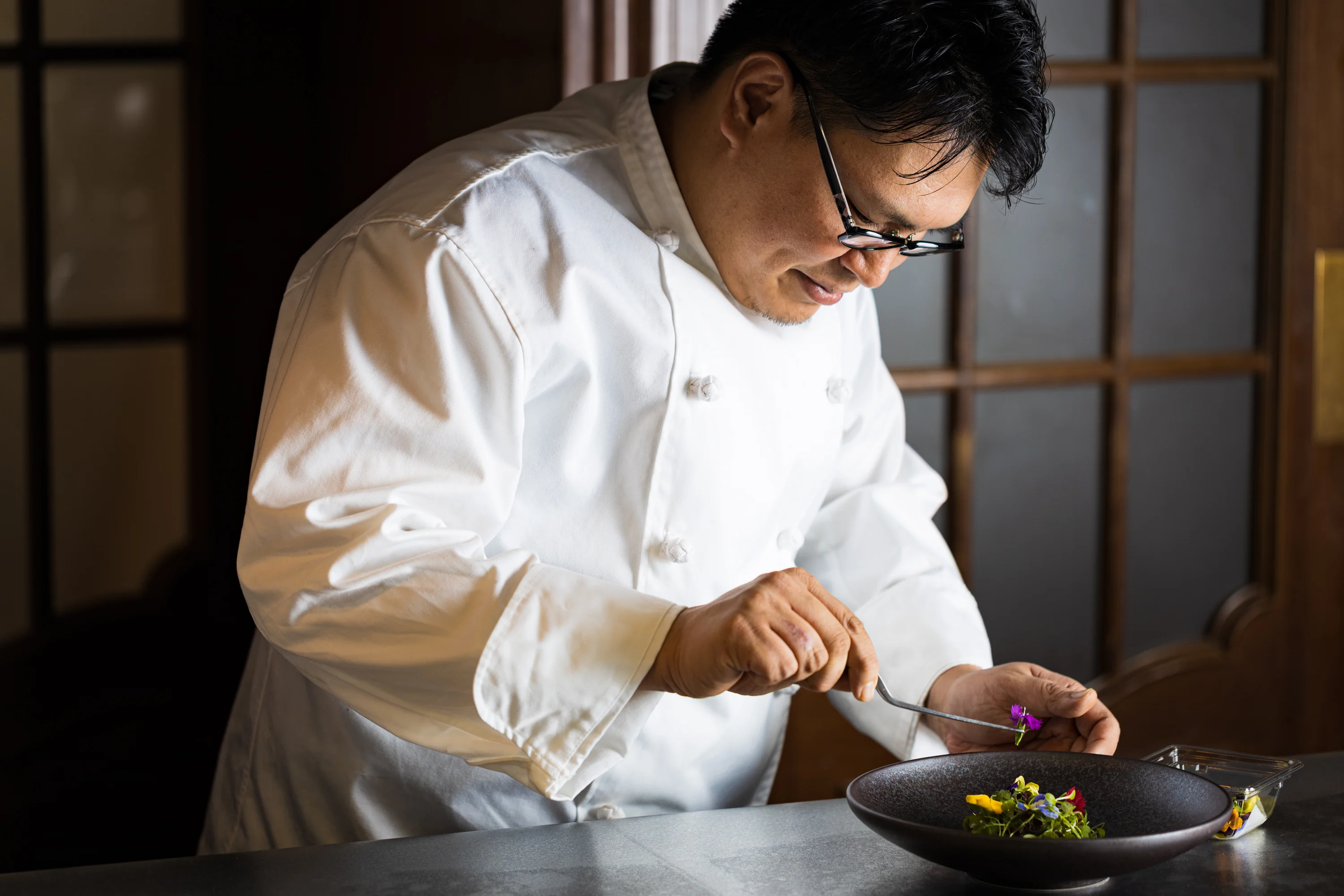 A chef carefully finishing a plated dish with edible flowers.