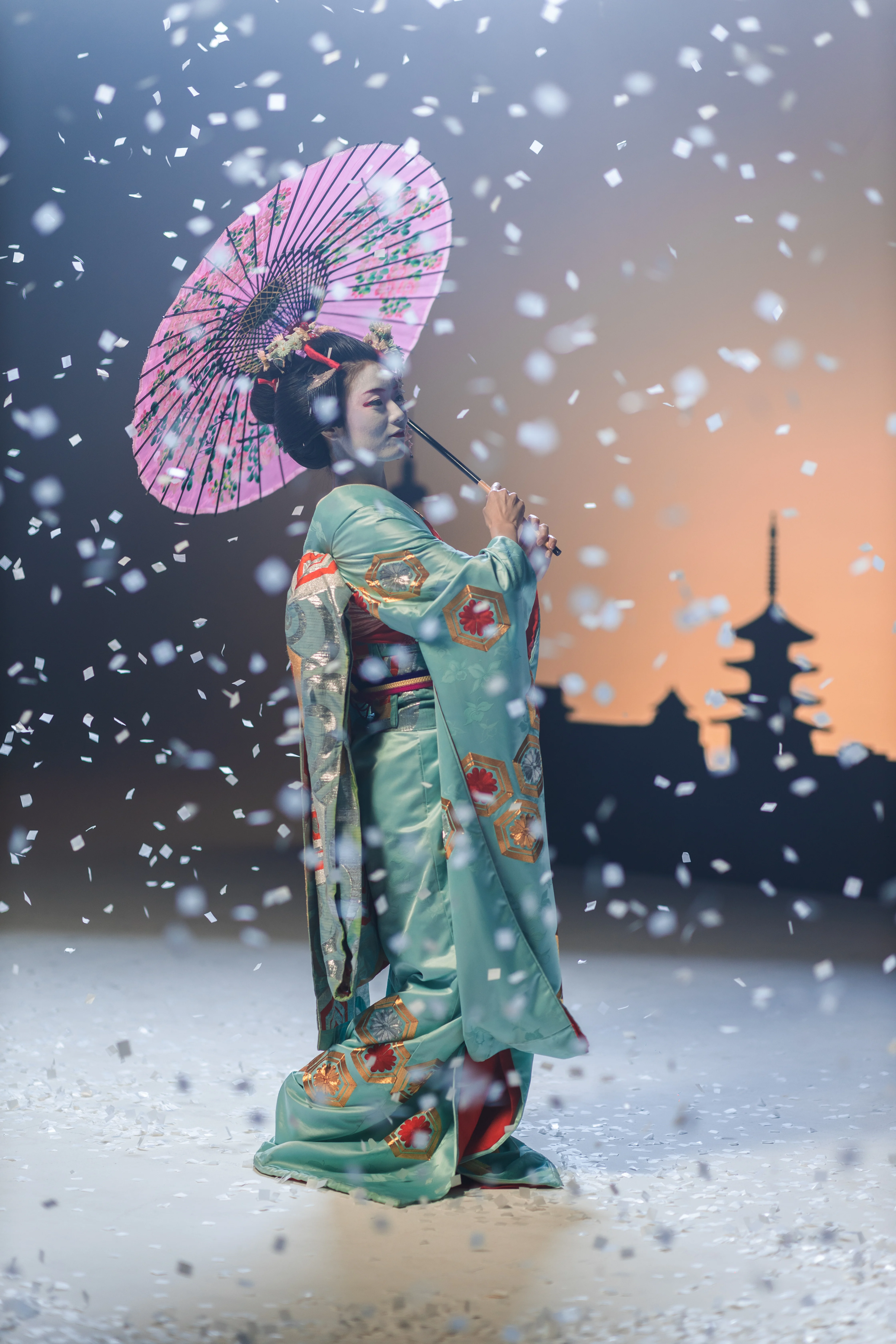 A figure in traditional dress holding a red parasol in falling snow.