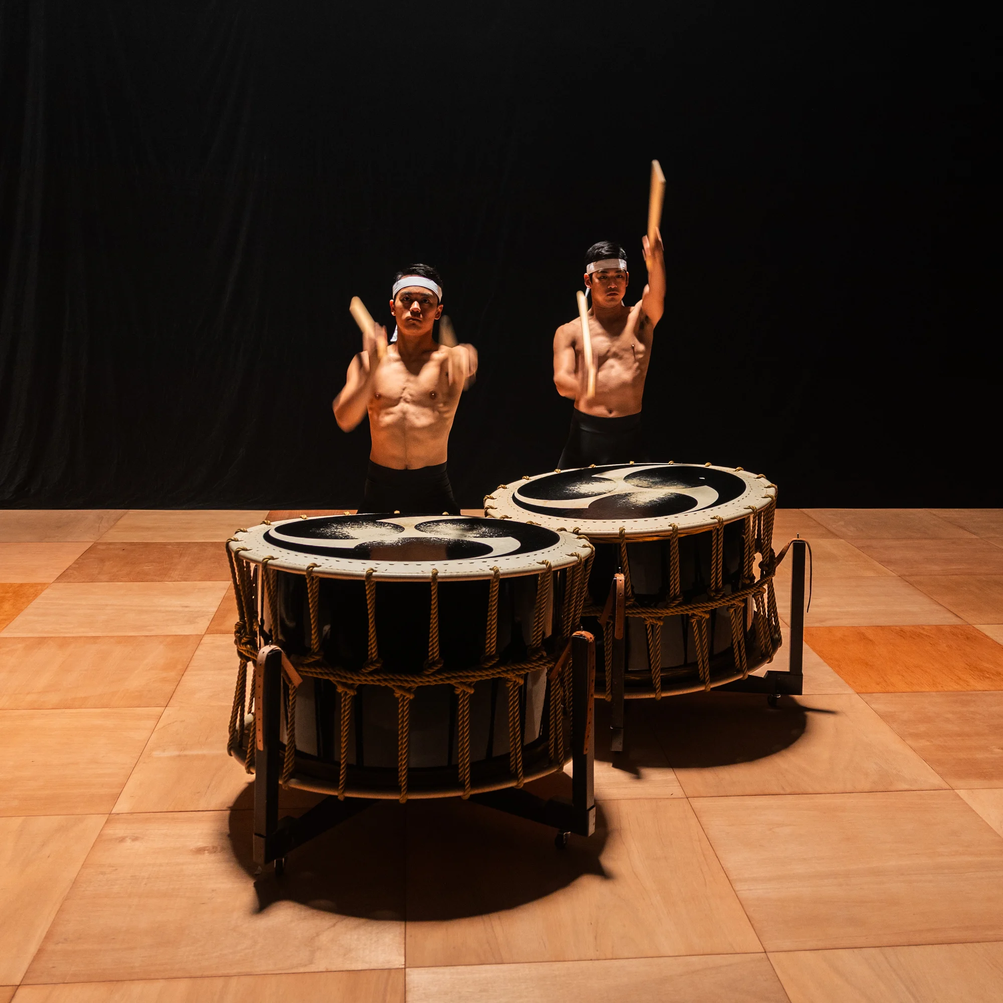 Taiko drummers performing together on a dark stage.